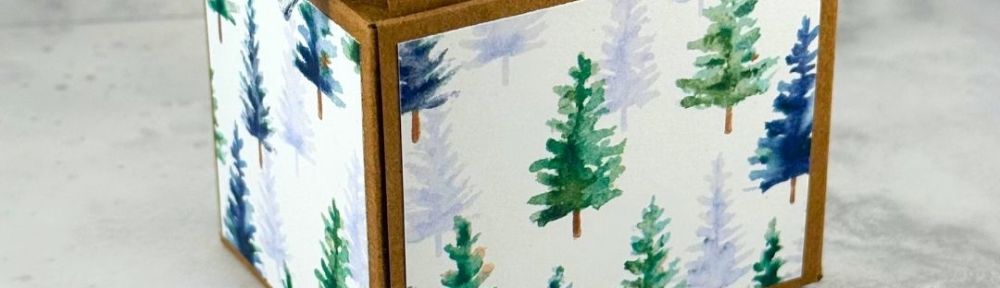 A small Kraft box covered with blue and green holiday designs and the sentiment "Holly Jolly Greetings"
